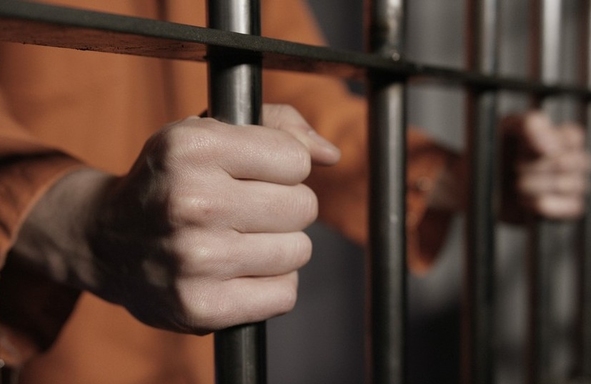 un hombre se sostiene de las barras de una celda de cárcel