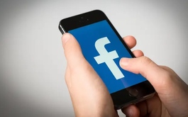 una persona sosteniendo un celular con el logo de facebook