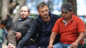 un hombre toca a otras personas en una banca de parque