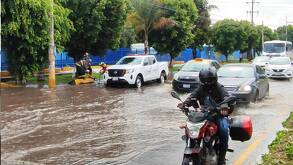 autos y una motociclista en una calle inundada por lluvias