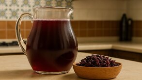 una jarra de agua de jamaica junto a flores de jamaica secas