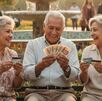 adultos de la tercera edad sentados en un parque con billetes en las manos