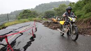 un hombre empuja una motocicleta en un camino dañado por deslaves en la sierra norte de puebla