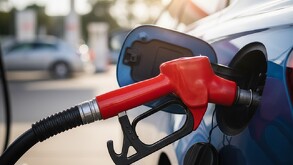 una manguera de gasolina despachando gasolina en una gasolinera a un auto azul
