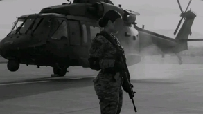 Mujer de la Guardia Nacional con un arma y de fondo un helicóptero.