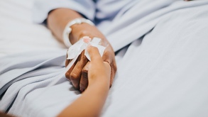 Mano de una mujer enferma recostada en una camilla de hospital.