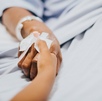 Mano de una mujer enferma recostada en una camilla de hospital.