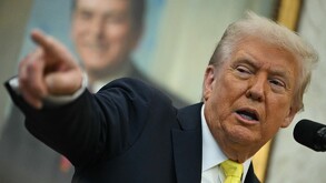 Donald Trump, con traje oscuro y corbata amarilla, habla en un atril mientras señala enfáticamente hacia la izquierda. Un retrato sonriente está borroso al fond