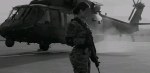 Mujer de la Guardia Nacional con un arma y de fondo un helicóptero.