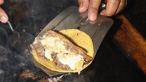 Taco de asada siendo preparado al carbón por un trabajador de Tacos Domingo en la Ciudad de México.