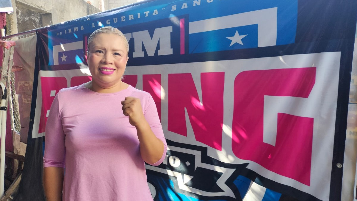 Mujer con blusa rosa, sonriendo y con el puño levantado en señal de fuerza, posa frente a una manta de Mujer con blusa rosa, sonriendo y con el puño levantado en señal de fuerza, posa frente a una manta de