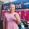 Mujer con blusa rosa, sonriendo y con el puño levantado en señal de fuerza, posa frente a una manta de Mujer con blusa rosa, sonriendo y con el puño levantado en señal de fuerza, posa frente a una manta de