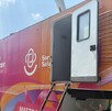 Vista lateral de una Unidad Móvil de Salud de color naranja y magenta con el mensaje Vista lateral de una Unidad Móvil de Salud de color naranja y magenta con el mensaje