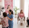 Escena en un centro de salud durante el Octubre Rosa. Una técnica realiza una mamografía, mientras una doctora conversa con una paciente en un área de espera. Escena en un centro de salud durante el Octubre Rosa. Una técnica realiza una mamografía, mientras una doctora conversa con una paciente en un área de espera.