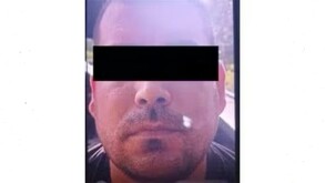 Primer plano de un hombre con barba corta, cara redonda y cabello oscuro. Una barra negra horizontal censura sus ojos. La iluminación es muy fuerte