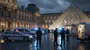 Escena nocturna y lluviosa en el Museo del Louvre en París. Varios policías armados y patrullas con luces azules bloquean la entrada de la pirámide de cristal.