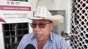 Primer plano de un hombre de mediana edad, campesino con sombrero de palma y lentes oscuros, hablando con expresión de indignación frente a un cartel