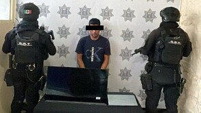 En la imagen aparece un hombre con playera azul, acompañado de dos policías a los que no se les ve la cara.