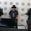 En la imagen aparece un hombre con playera azul, acompañado de dos policías a los que no se les ve la cara.