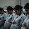 Cuatro mujeres embarazadas migrantes con uniformes grises idénticos, sentadas en una hilera tocando sus vientres. El fondo sombrío sugiere una detención Cuatro mujeres embarazadas migrantes con uniformes grises idénticos, sentadas en una hilera tocando sus vientres. El fondo sombrío sugiere una detención