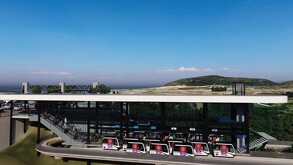 Renders de una estación de tren ligero elevada y futurista, con varios vagones blancos en una vía. Se ven escaleras y pasajeros. El paisaje circundante