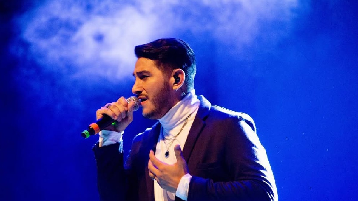 En la imagen aparece Joan Sebastián Alarcón, quien se encuentra con un atuendo en color negro sosteniendo un micrófono, en lo que parece ser un concierto. En la imagen aparece Joan Sebastián Alarcón, quien se encuentra con un atuendo en color negro sosteniendo un micrófono, en lo que parece ser un concierto.