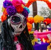 Primer plano de una figura de La Catrina con un cráneo decorado y una corona de flores de papel brillantes (rosa, morado, azul). Un altar del Día de Muertos Primer plano de una figura de La Catrina con un cráneo decorado y una corona de flores de papel brillantes (rosa, morado, azul). Un altar del Día de Muertos