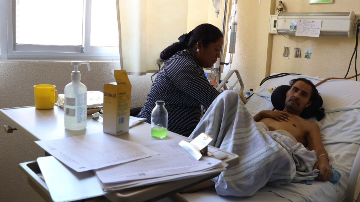 Hombre hospitalizado siendo asistido por una de sus familiares en un nosocomio del IMSS-Bienestar.