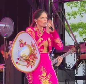 En la imagen se puede ver a Ana Bárbara con una vestimenta de charro en color rosa fiusha y con la cara enojada al intentar cantar con su micrófono descompuesto