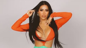 En la imagen aparece Kim Shantal con un atuendo en color naranja, posando con las manos elevadas a la cara.