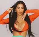 En la imagen aparece Kim Shantal con un atuendo en color naranja, posando con las manos elevadas a la cara.