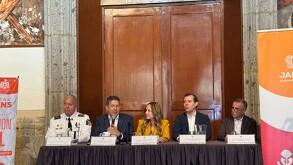 Una mujer de mediana edad con un uniforme de la policía vial y chaleco naranja, cruza una calle señalizada. Está dirigiendo el tráfico con el brazo extendido, m