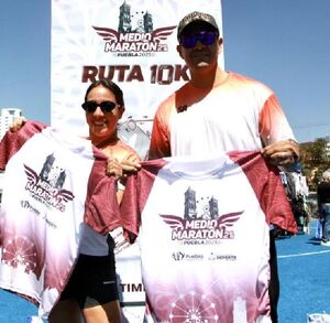 un hombre y una mujer mostrando una playera del medio maratón puebla 2025 un hombre y una mujer mostrando una playera del medio maratón puebla 2025