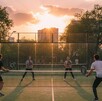 Pista de pádel en Guadalajara al atardecer. Cuatro jóvenes, hombres y mujeres, juegan con palas de colores, rodeados de muros de vidrio. El sol proyecta una luz Pista de pádel en Guadalajara al atardecer. Cuatro jóvenes, hombres y mujeres, juegan con palas de colores, rodeados de muros de vidrio. El sol proyecta una luz