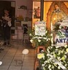 Un funeral con un ataúd cubierto y arreglos florales rodeados por una ofrenda de la Virgen de Guadalupe y globos. Varias personas, principalmente mujeres. Un funeral con un ataúd cubierto y arreglos florales rodeados por una ofrenda de la Virgen de Guadalupe y globos. Varias personas, principalmente mujeres.