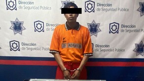 En la imagen se pude ver a un hombre esposado y con la cara cubierta, con una playera naranja y pantalón rojo.