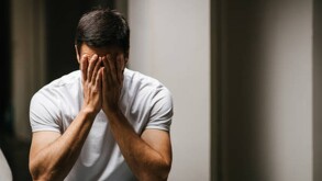 Hombre triste con las manos tapando sus ojos.