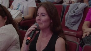 La política Natalia Montaño Ruelas sonríe mientras habla por un micrófono de mano. Tiene cabello castaño rojizo y un vestido negro. Una frase de diálogo azul di