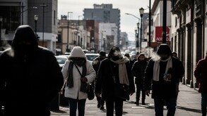 En la imagen aparece un grupo de personas caminando con chamarras y gorros debido al frío