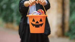 Niño usando disfraz y sosteniendo una calabaza de Halloween llena de dulces tras pedir dulce o truco