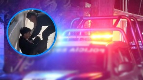 En la imagen se puede ver un vehiculo de la policia con las torretas prendidas, y en la misma imagen se ve a un hombre siendo arrestado.