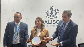 Tres personas (dos hombres en traje y corbata, y una mujer en una chaqueta color camel) están de pie frente a una pared con el logotipo del Gobierno de Jalisco.