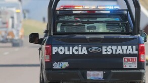 Patrulla de la policía estatal de Durango vista desde su parte trasera mientras circula en una carretera, con un tráiler al frente.