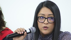Mujer con cabello negro y lentes sosteniendo un micrófono con la mano.