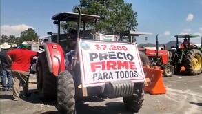 Tractor bloqueando carretera en Michoacán con manta que tiene la exigencia de 7 mil 200 pesos por tonelada de maíz.