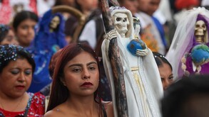 Mujer caminando con una imagen de la santa muerte en la mano.
