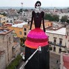 Catrina gigante, un esqueleto femenino elegantemente vestido con un sombrero de flores, elevándose sobre los edificios de un pueblo o ciudad mexicana, en proces Catrina gigante, un esqueleto femenino elegantemente vestido con un sombrero de flores, elevándose sobre los edificios de un pueblo o ciudad mexicana, en proces