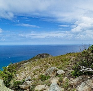 Isla Lizard en Australia, vista desde un acantilado, al fondo se aprecia un par de barcos, y nubes en el cielo.