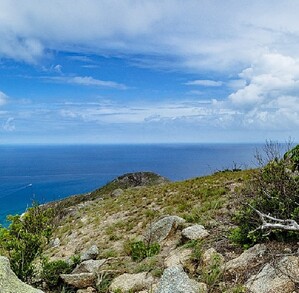 Isla Lizard en Australia, vista desde un acantilado, al fondo se aprecia un par de barcos, y nubes en el cielo.