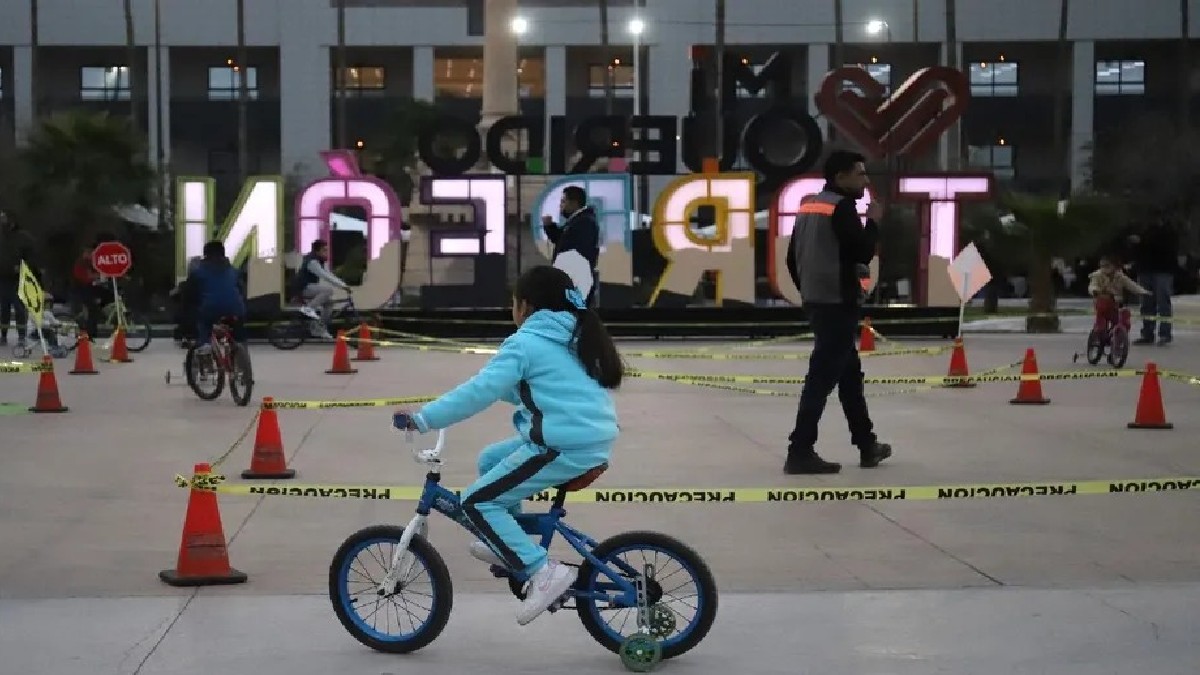 Niña vestida de azul cielo en la Plaza Mayor de Torreón paseando en su bicicleta.